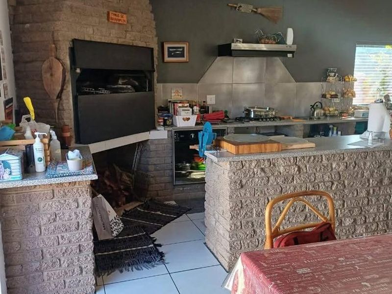 Open-plan living area featuring a prominent brick fireplace with built-in braai, stone-clad breakfast counter, and tiled flooring throughout.