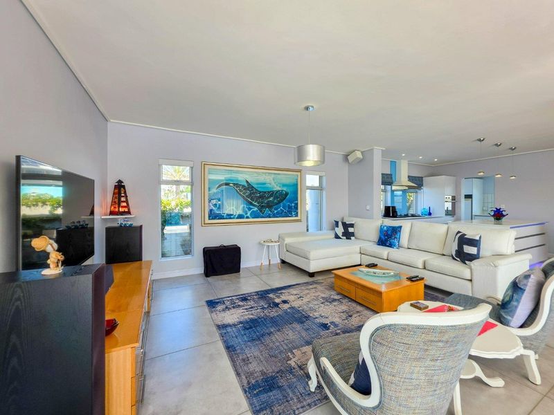 Spacious open-plan living area featuring tiled floors, modern lighting, and a seamless transition into a well-equipped kitchen with built-in cabinetry and appliances.
