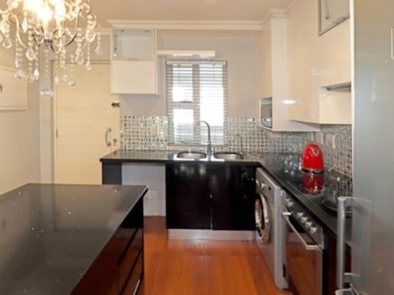 Modern kitchen featuring high-gloss cabinetry, granite countertops, a central island, mosaic backsplash, and integrated appliances including an oven and washing machine.