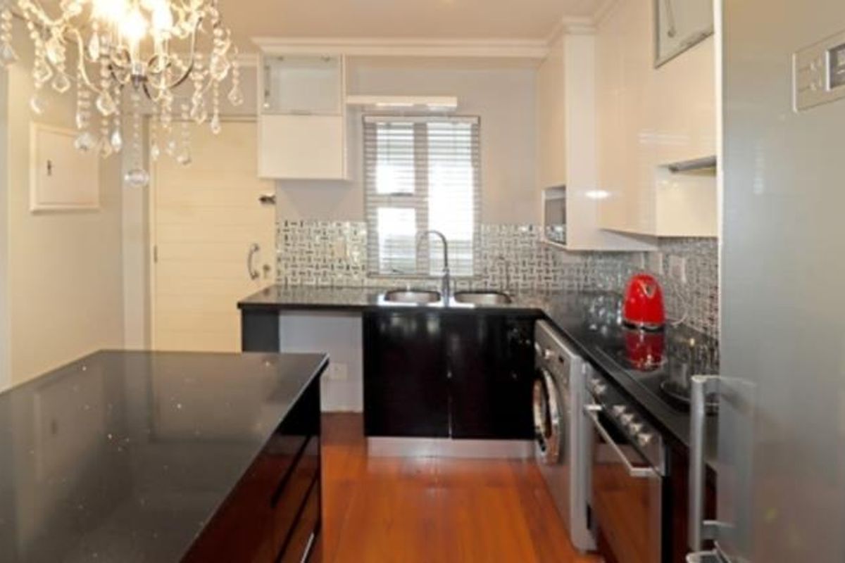 Modern kitchen featuring high-gloss cabinetry, granite countertops, a central island, mosaic backsplash, and integrated appliances including an oven and washing machine.