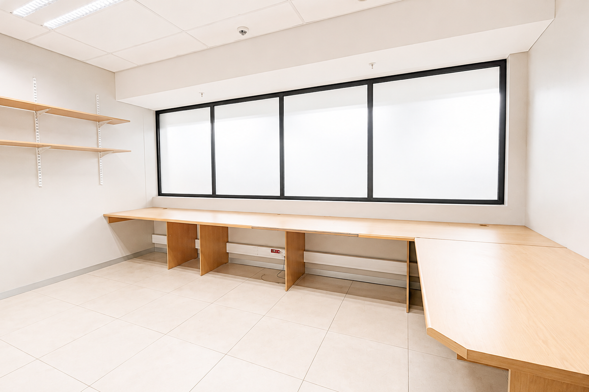 A bright, empty office space featuring a large built-in desk, wall-mounted shelving, tiled flooring, and a suspended ceiling with integrated lighting.