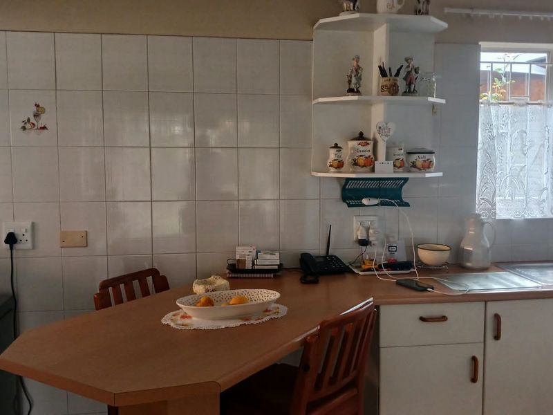 A functional kitchen featuring a laminate breakfast nook, tiled splashback, built-in corner shelving, and a stainless steel sink with ample cabinetry.