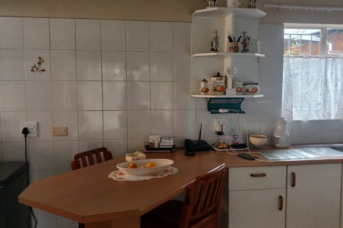 A functional kitchen featuring a laminate breakfast nook, tiled splashback, built-in corner shelving, and a stainless steel sink with ample cabinetry.