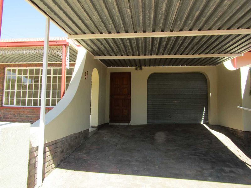 A covered carport area featuring a corrugated metal roof, brick paving, and a secure roller shutter door leading to the garage entrance.