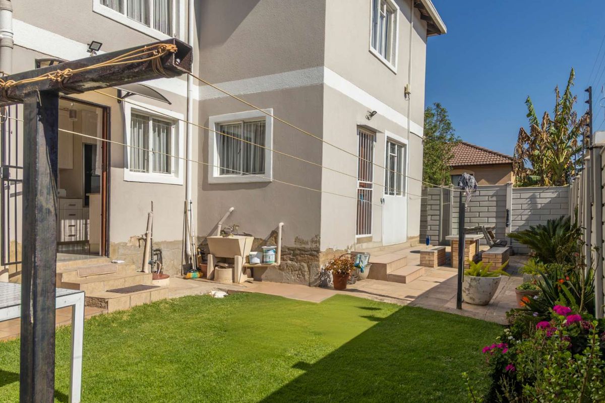Rear exterior view of the property featuring a paved patio area, small lawn, and a built-in laundry sink against the house wall.