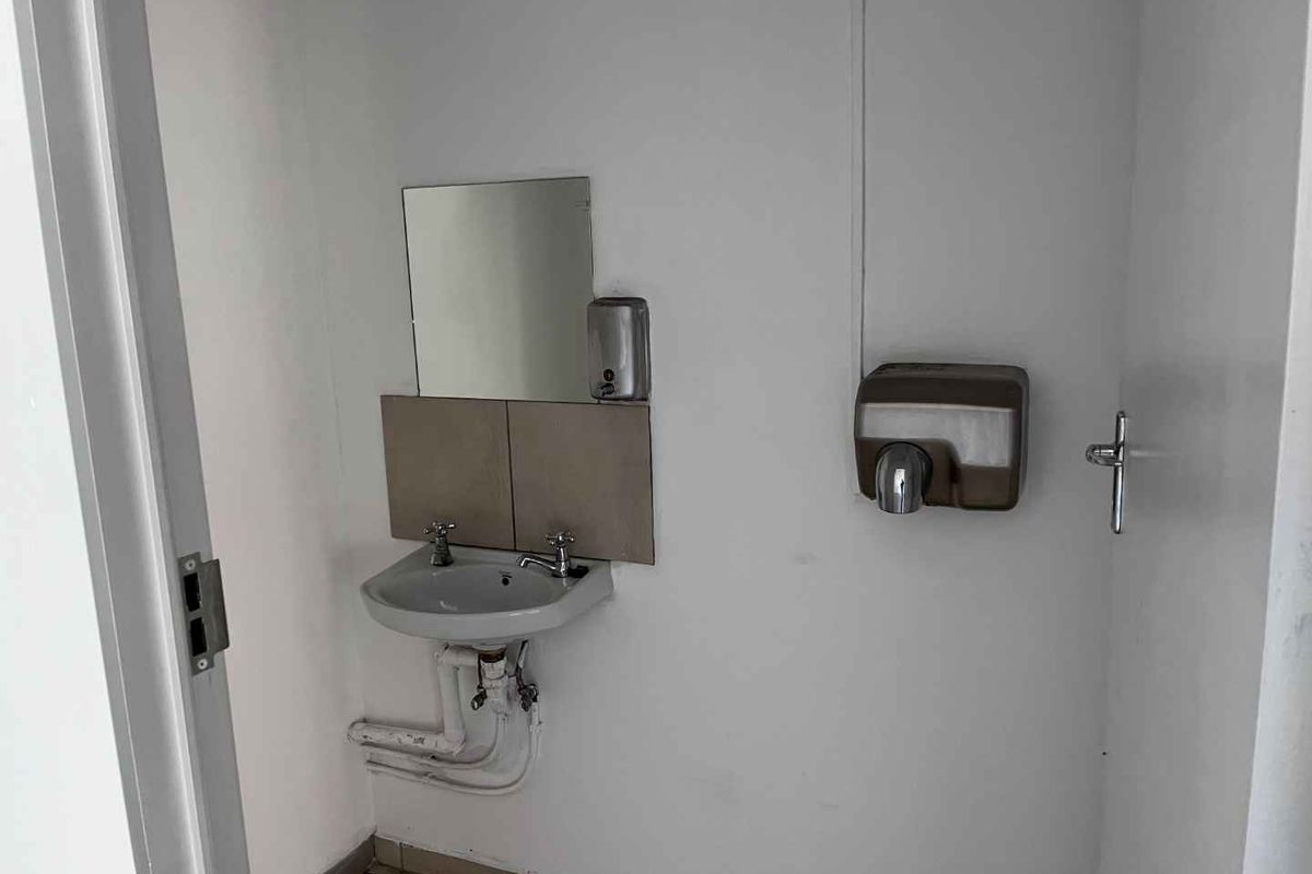 A functional commercial restroom facility featuring a wall-mounted basin, mirror, and soap dispenser, with basic utility finishes.