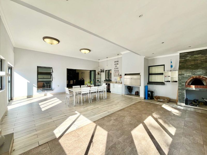 Spacious open-plan entertainment area featuring a built-in braai, pizza oven, and kitchenette, with direct access to outdoor spaces through large sliding doors.