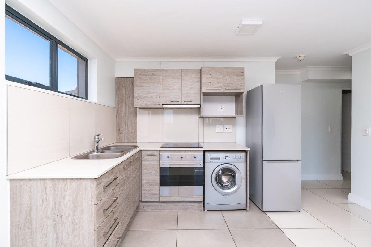Modern kitchen featuring light wood-grain cabinetry, integrated oven and hob, tiled splashbacks, and neutral floor tiles in a clean, well-maintained apartment setting.