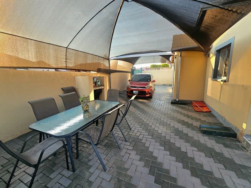 Covered outdoor patio area featuring a shade sail, paved flooring, and a built-in braai, suitable for outdoor dining and entertainment.