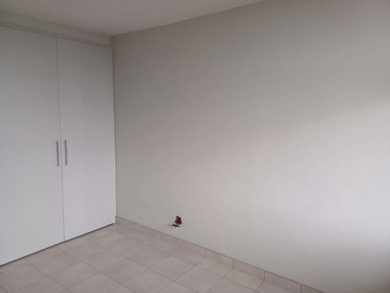 An empty bedroom featuring neutral tiled flooring and built-in cupboards, with exposed electrical wiring requiring attention.
