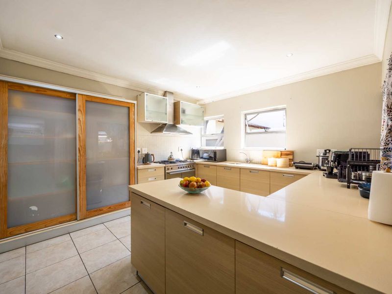 Modern kitchen featuring light wood cabinetry, stone countertops, gas hob, stainless steel oven, and large sliding pantry doors with frosted glass panels.