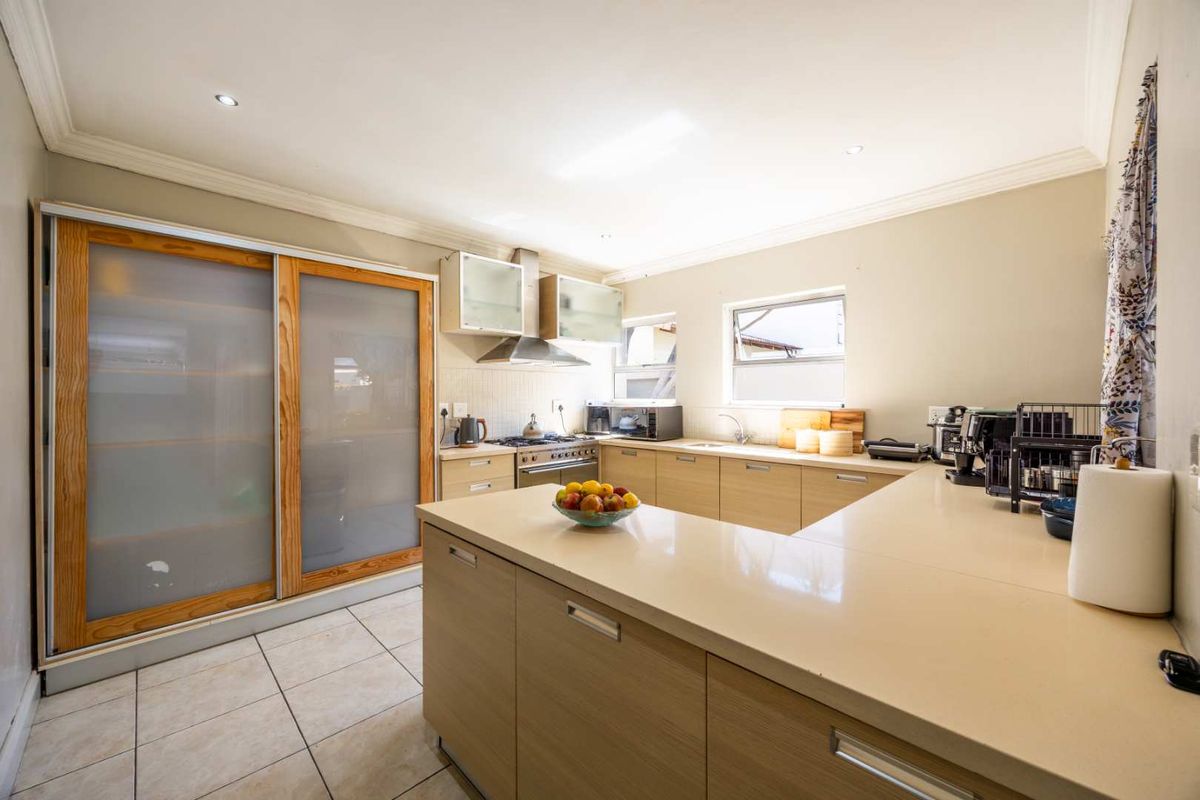 Modern kitchen featuring light wood cabinetry, stone countertops, gas hob, stainless steel oven, and large sliding pantry doors with frosted glass panels.