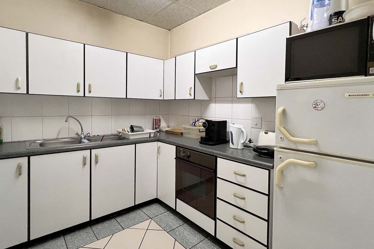 A functional industrial kitchen featuring white cabinetry, tiled backsplash, integrated oven, and durable tiled flooring, providing a practical workspace for staff.