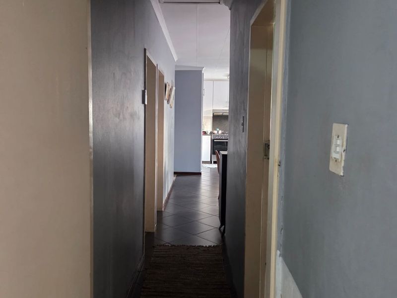 A narrow interior hallway with tiled flooring and visible wall wear, leading towards the kitchen area.