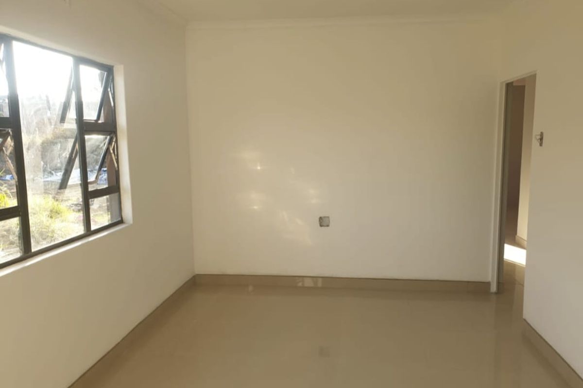 A clean, empty bedroom featuring neutral tiled flooring and large aluminium-framed windows, providing a bright and versatile space ready for personalization.