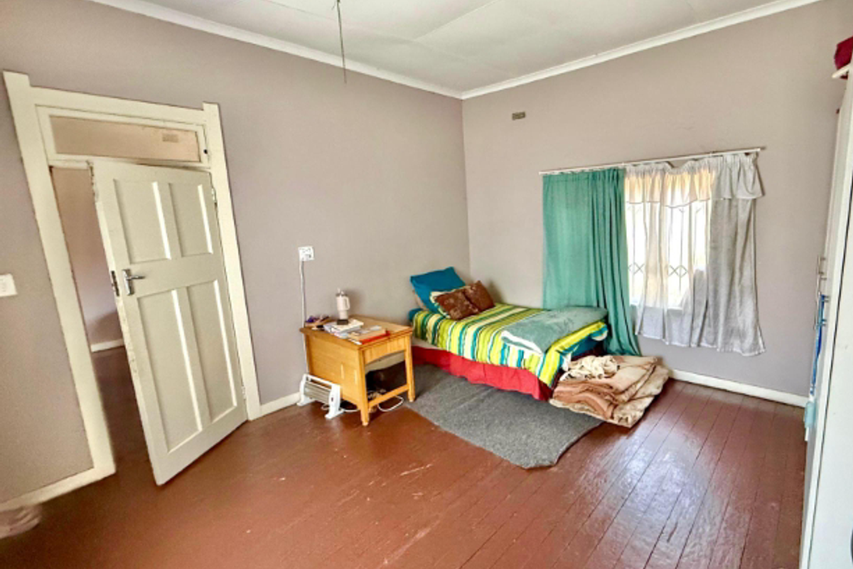 A bedroom featuring original timber flooring, a classic panelled door, and a window with security bars.