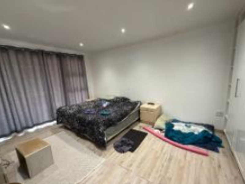 A spacious bedroom featuring light laminate flooring, recessed downlighting, and built-in cupboards, with access to an outdoor area via a large sliding glass door.