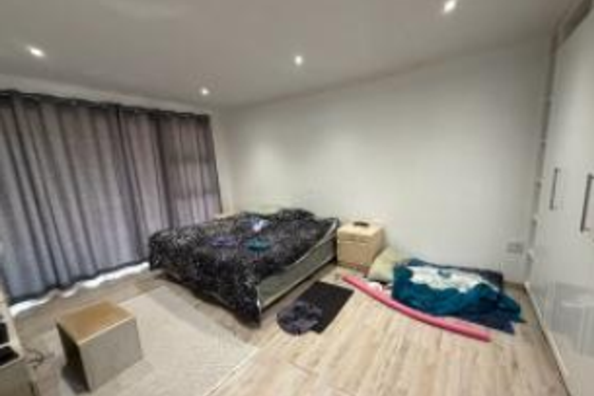 A spacious bedroom featuring light laminate flooring, recessed downlighting, and built-in cupboards, with access to an outdoor area via a large sliding glass door.