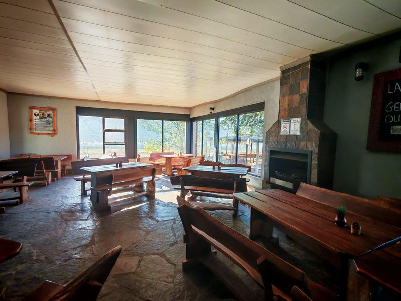 Spacious open-plan dining area featuring rustic stone flooring, a built-in fireplace with tiled surround, and large windows offering natural light and outdoor views.