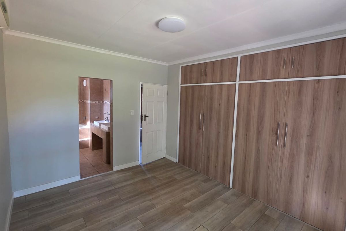 A spacious bedroom featuring wood-look tile flooring, extensive built-in wooden cabinetry, and an adjoining en-suite bathroom.