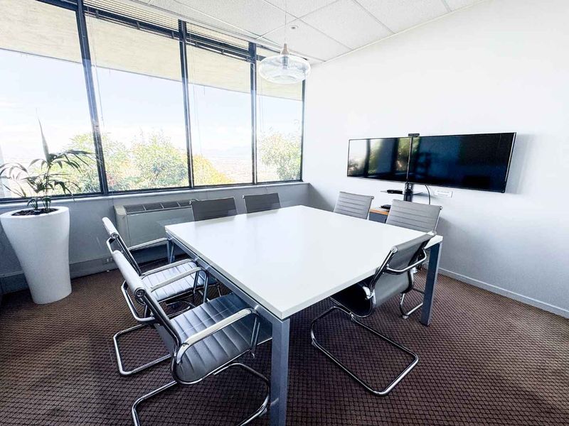 A professional office meeting room featuring large windows with natural light, suspended ceiling, and wall-mounted display screens for presentations.