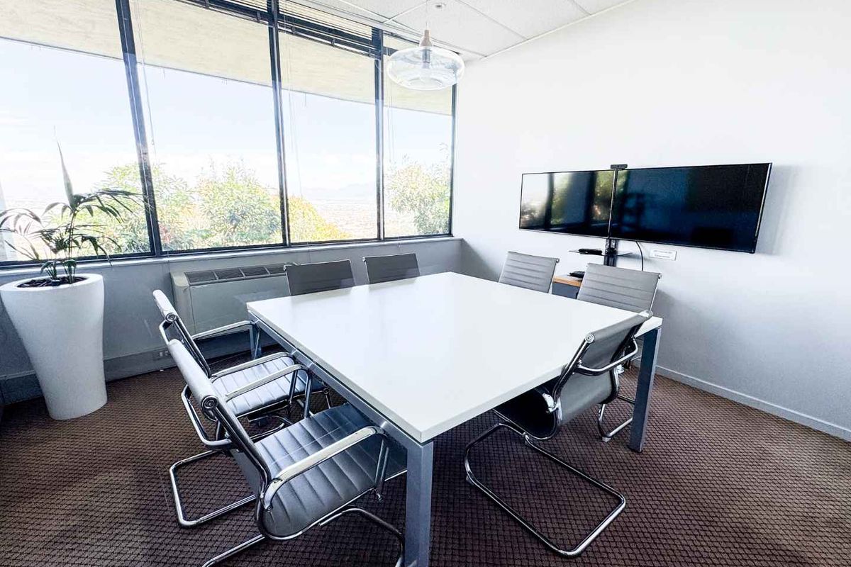 A professional office meeting room featuring large windows with natural light, suspended ceiling, and wall-mounted display screens for presentations.