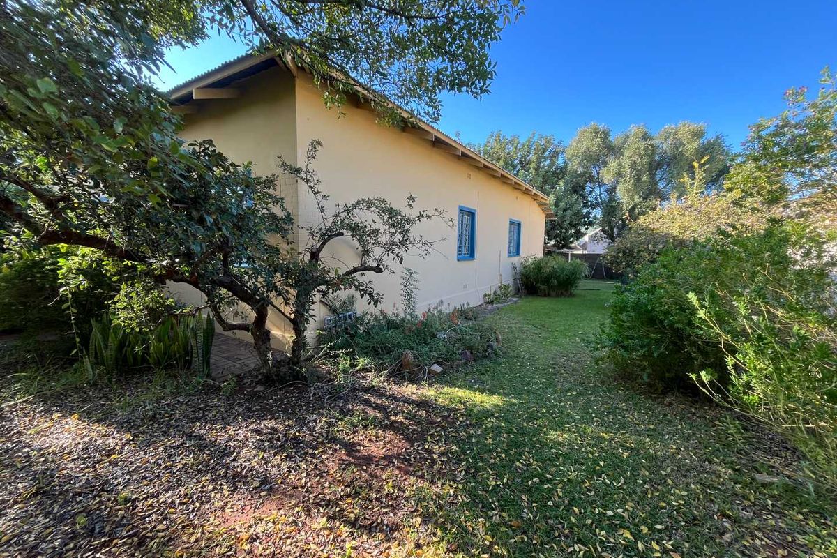 A view of the rear exterior of the house, featuring a garden area with established trees and lawn.