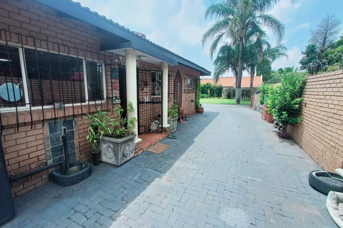 Side view of the property featuring a paved driveway, brick facade, covered entrance area, and security bars on windows.