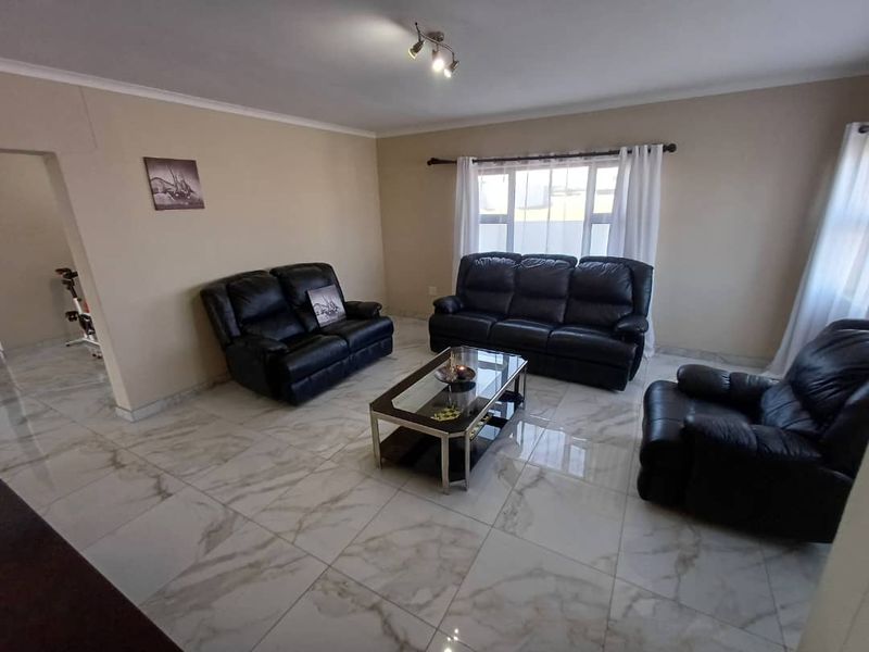 A spacious living room featuring large format marble-look floor tiles, neutral wall tones, and ample natural light through large windows.