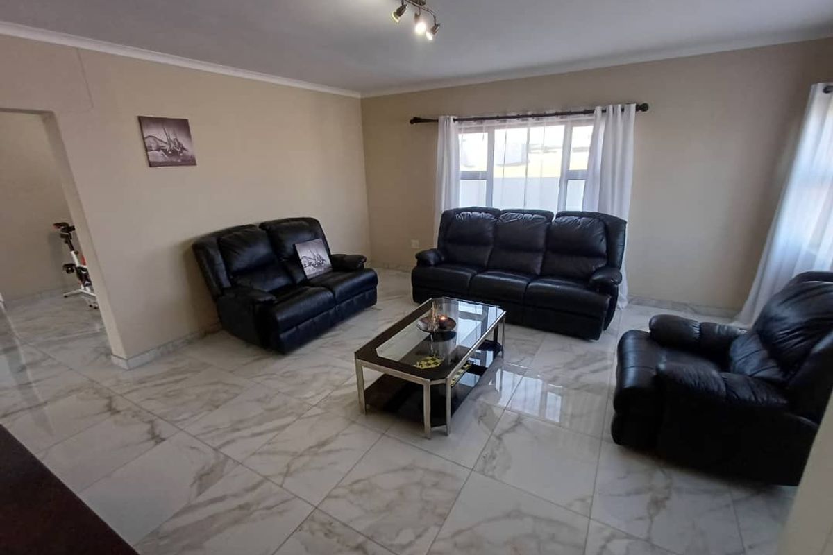 A spacious living room featuring large format marble-look floor tiles, neutral wall tones, and ample natural light through large windows.