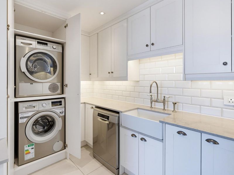 A modern, well-appointed laundry area featuring white shaker-style cabinetry, a farmhouse sink, subway tile backsplash, and integrated appliances.