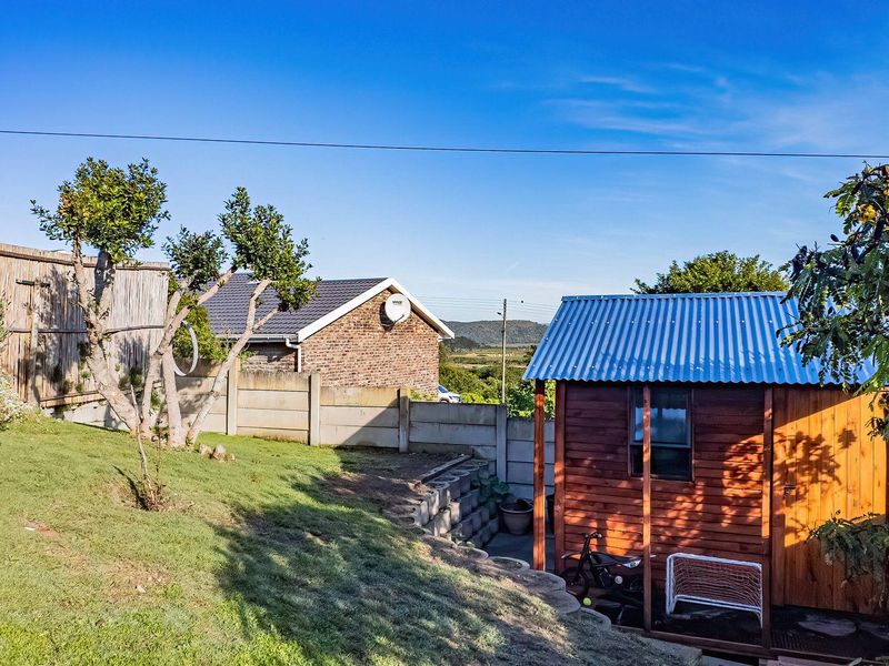 A backyard garden area featuring a timber shed with a corrugated metal roof, enclosed by precast concrete boundary walls and a retaining wall.