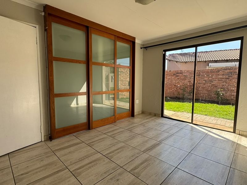 A bright, empty bedroom featuring tiled flooring, a built-in wooden wardrobe with frosted glass sliding doors, and direct access to the rear garden.
