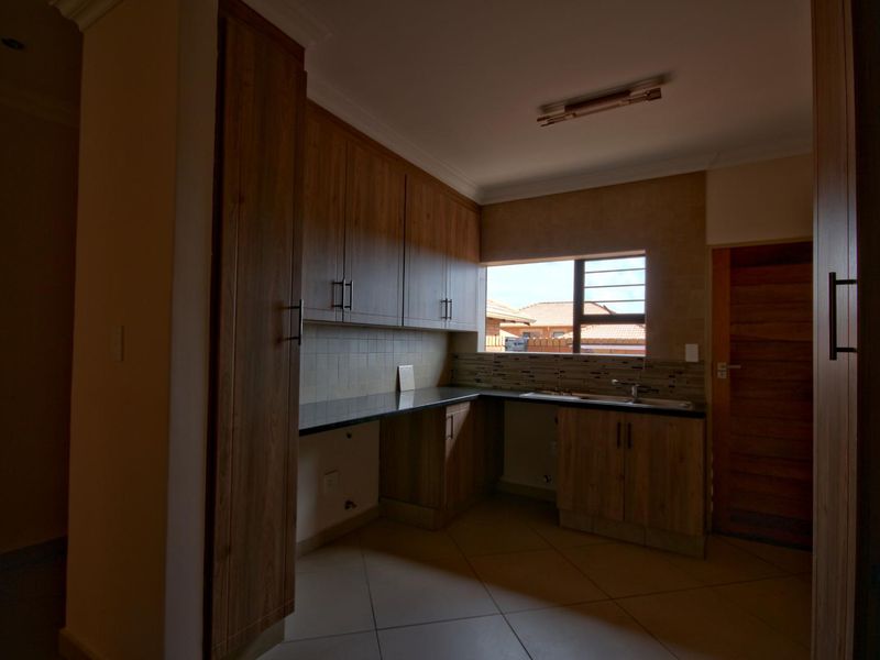 A functional kitchen featuring wood-look laminate cabinetry, dark granite countertops, tiled backsplash, and a double basin sink with neutral floor tiles.
