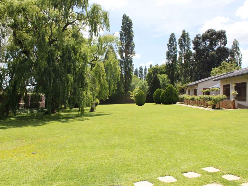 A spacious, well-maintained garden featuring a large lawn, mature trees, and stone-clad exterior wall of the cottage.