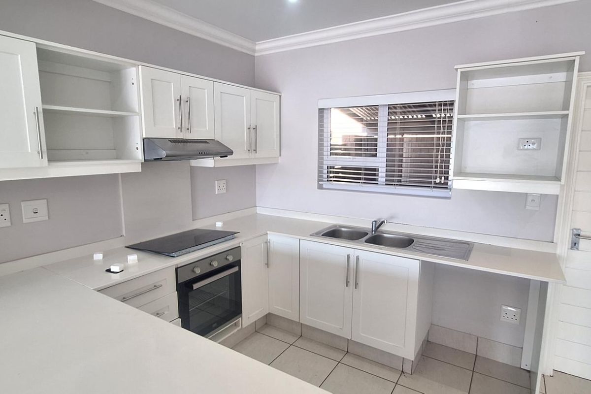 A clean, modern kitchen featuring white cabinetry, stone countertops, integrated oven and hob, and tiled flooring in a well-maintained townhouse setting.
