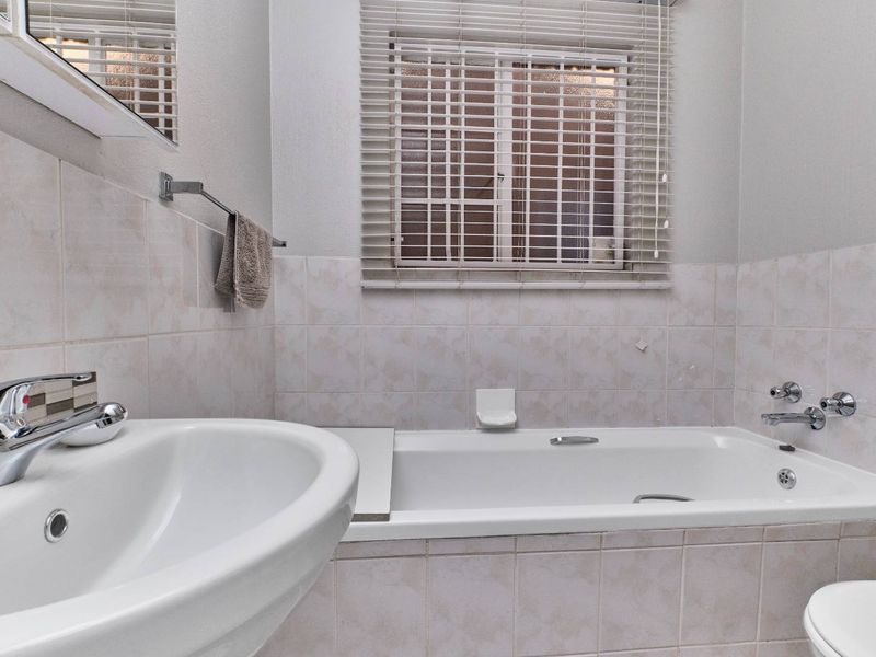 A functional bathroom featuring a built-in bathtub, pedestal washbasin, chrome fixtures, and tiled wall finishes with a window for natural light.
