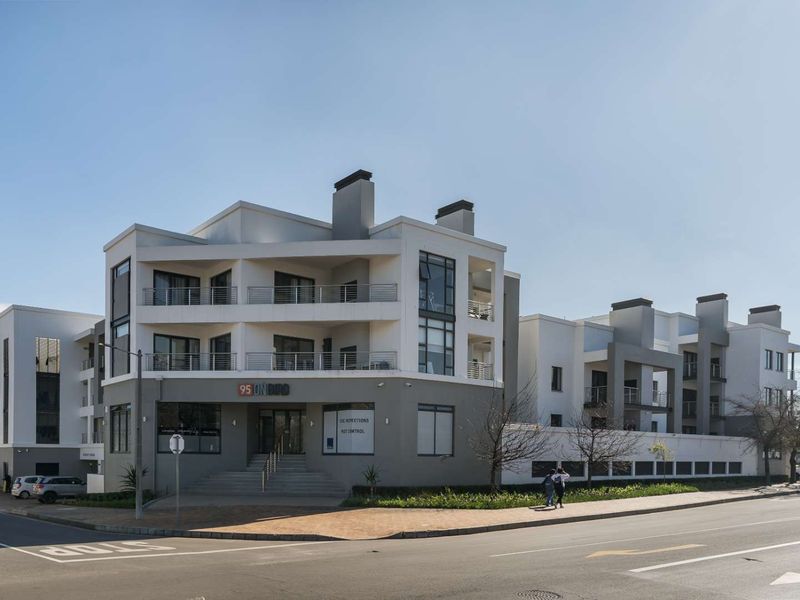 A modern multi-story apartment building exterior featuring clean architectural lines, private balconies, and a prominent street-level entrance.
