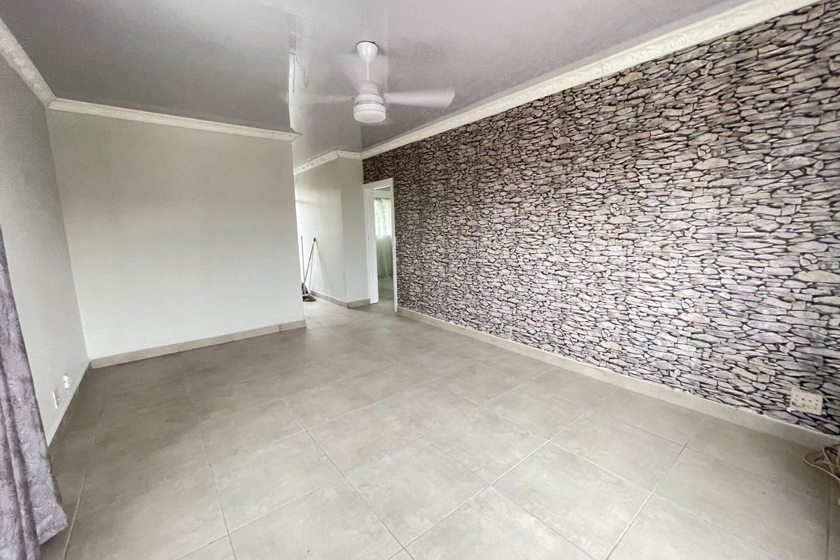 An empty living room featuring large floor tiles, a ceiling fan, and a prominent stone-effect feature wall.