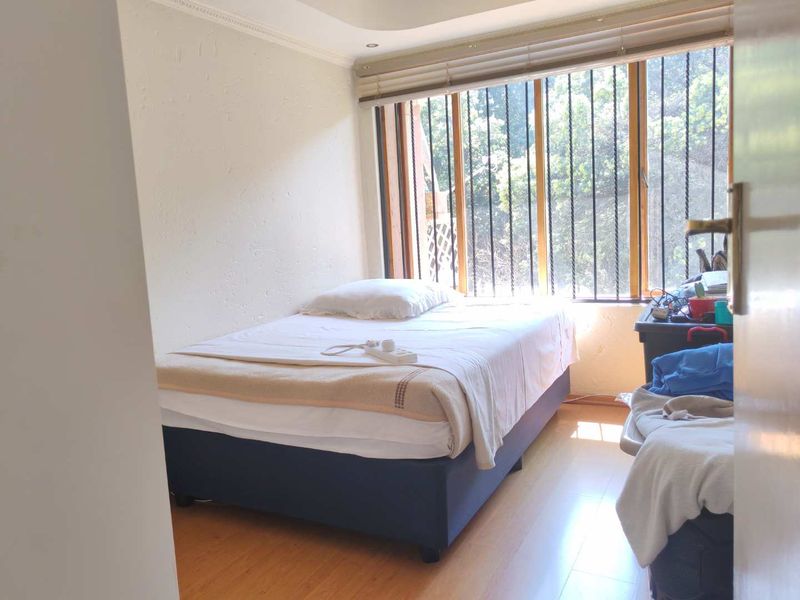 A bedroom featuring laminate flooring, window blinds, and security bars on the windows, providing a functional space with natural light.