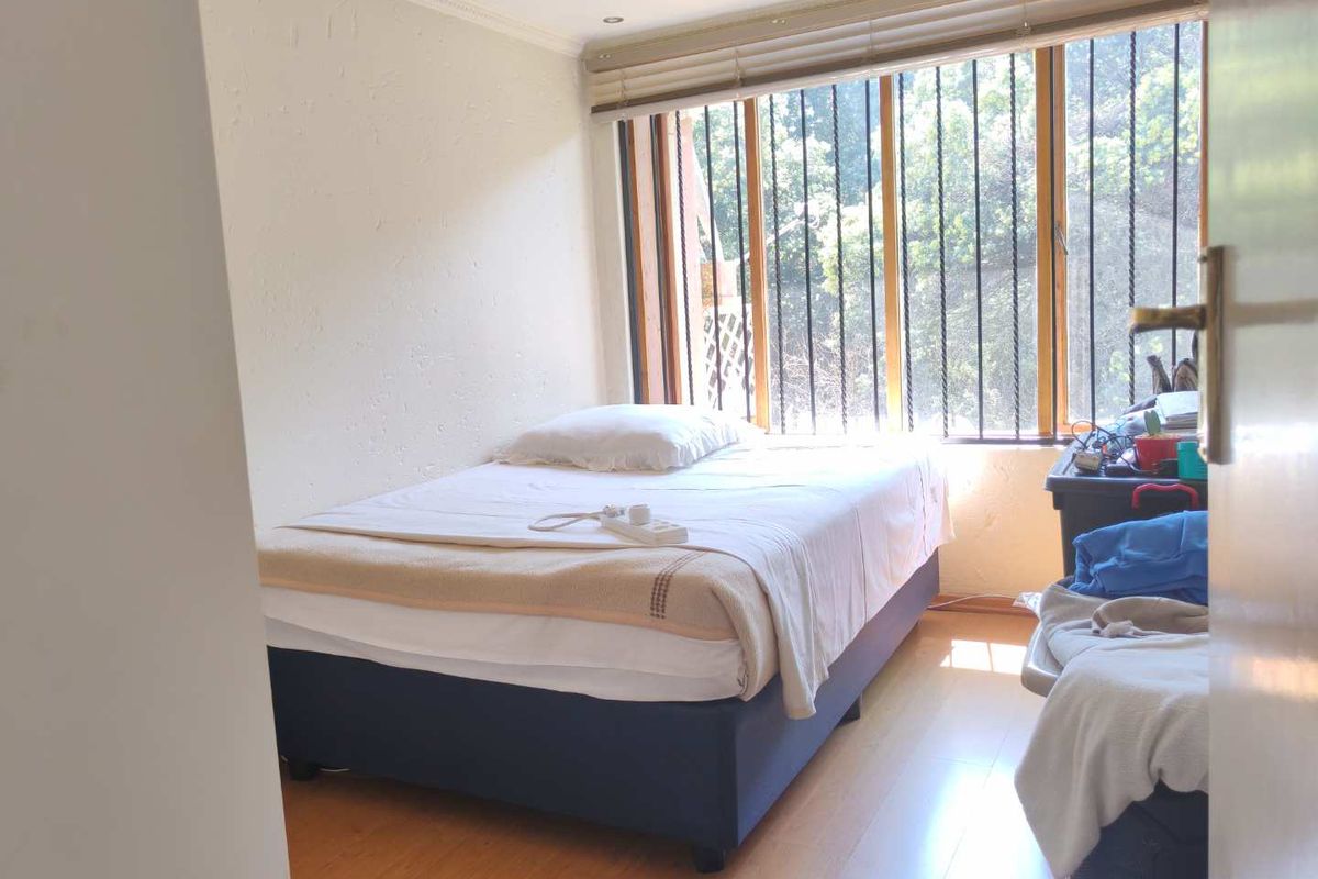 A bedroom featuring laminate flooring, window blinds, and security bars on the windows, providing a functional space with natural light.