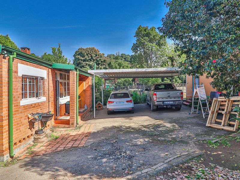 Rear exterior view of the property featuring a brick facade, a covered carport, and a concrete driveway area.