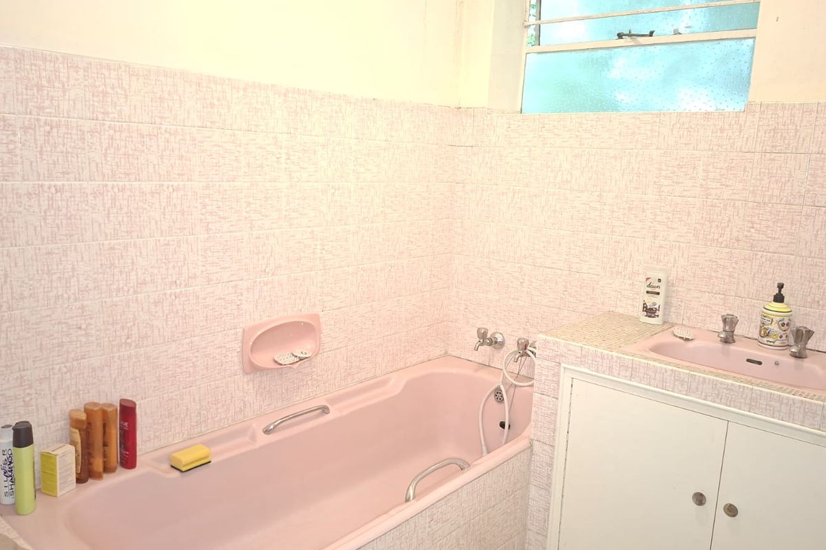 A dated bathroom featuring a pink built-in bathtub, integrated vanity sink, and textured wall tiling with a louvered window.