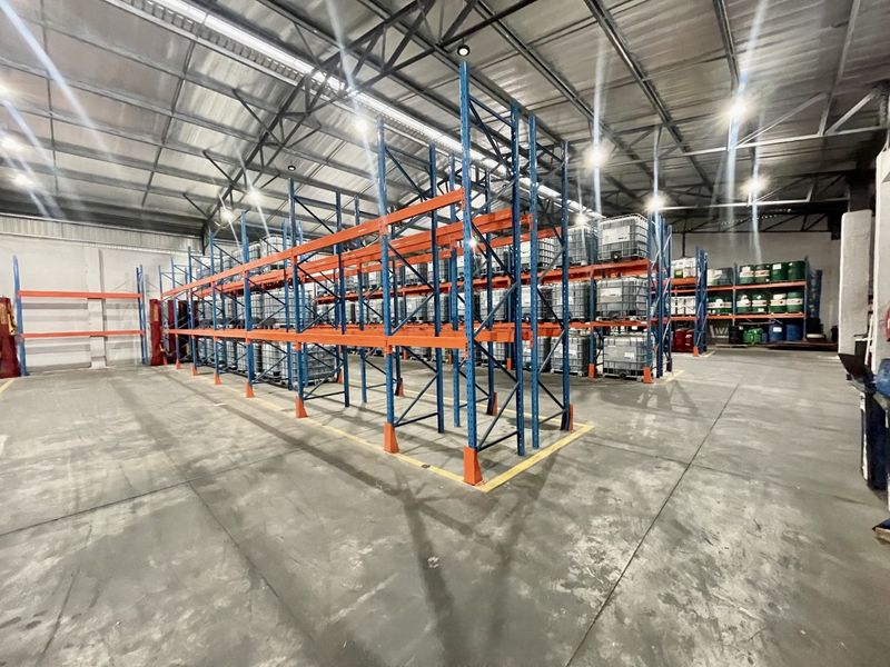 Spacious industrial warehouse featuring high-bay lighting, exposed steel roof trusses, and extensive heavy-duty racking systems on a durable concrete floor.