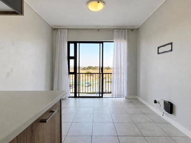 An open-plan living area featuring tiled flooring, a kitchen countertop, and a sliding glass door leading to a balcony with exterior views.
