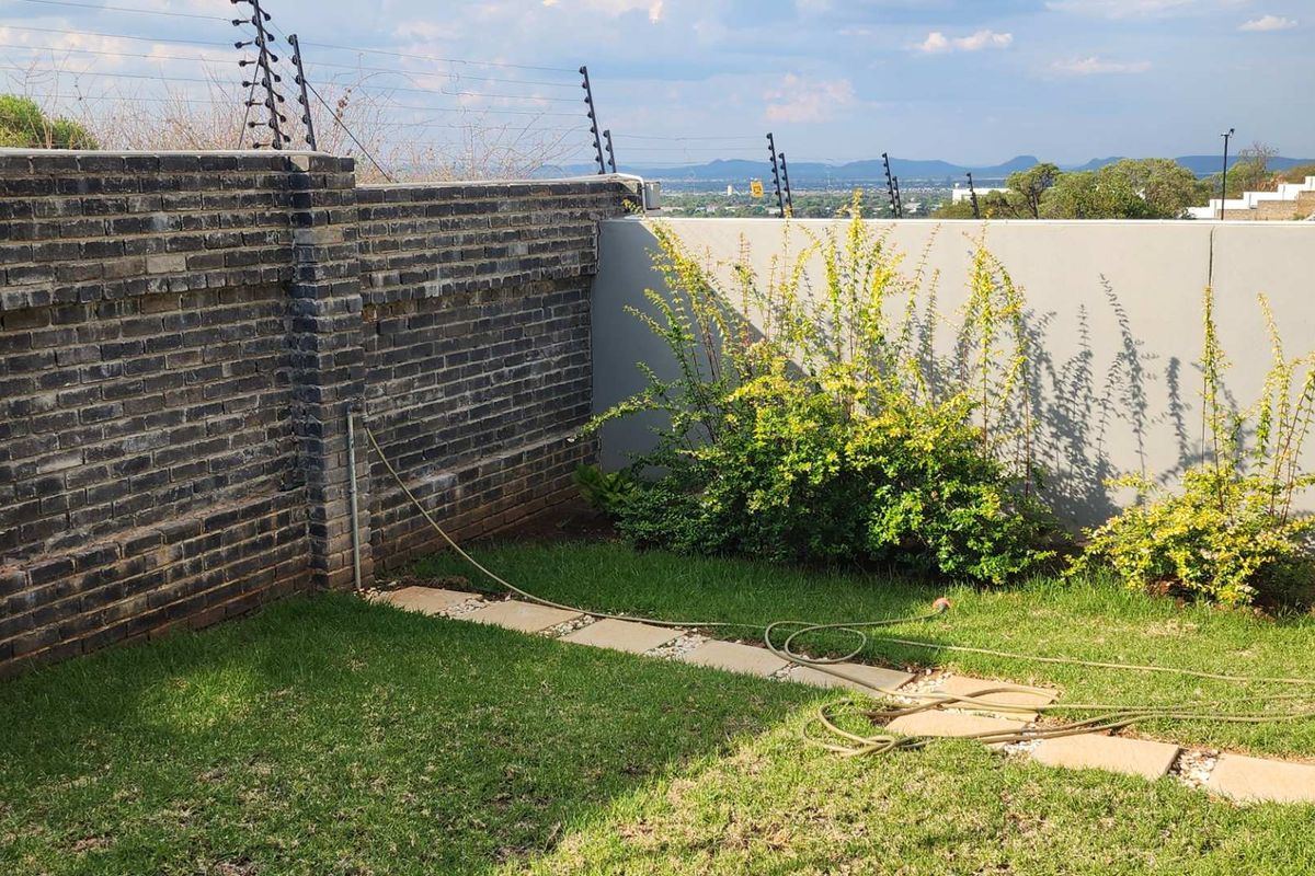 A private rear garden area featuring a brick boundary wall, electric fencing, and a paved pathway leading through the lawn.