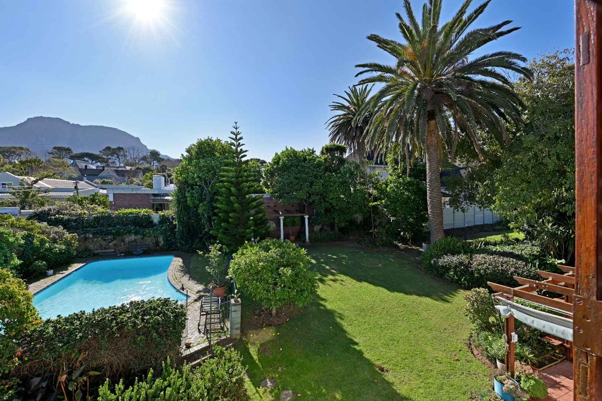 A spacious rear garden featuring a swimming pool, manicured lawn, mature trees, and a wooden pergola, offering a serene outdoor living space.