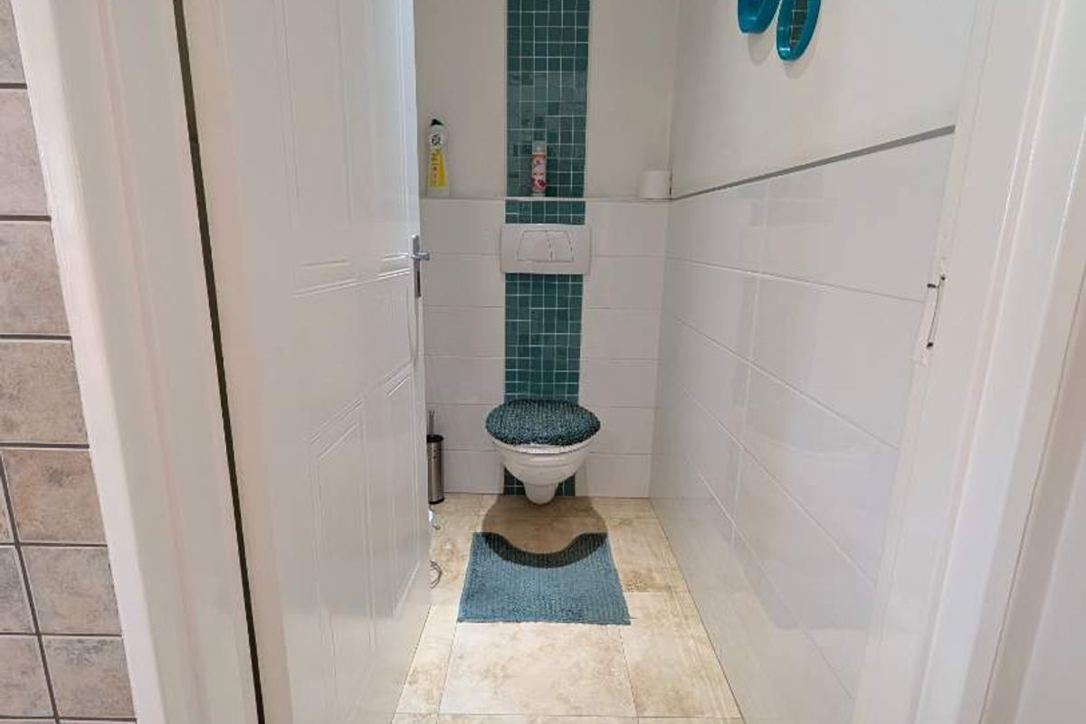 A compact bathroom featuring a wall-mounted toilet with a concealed cistern, accented by a vertical strip of blue mosaic tiles.