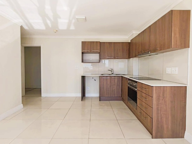 Modern kitchen featuring wood-finish cabinetry, integrated oven and hob, tiled flooring, and neutral walls, offering a clean and functional space.