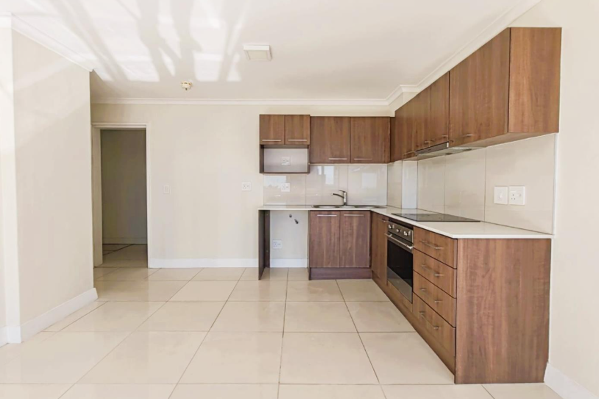 Modern kitchen featuring wood-finish cabinetry, integrated oven and hob, tiled flooring, and neutral walls, offering a clean and functional space.